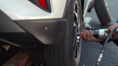 mechanic man using an electric drill to loosen the bolts of vehicle wheel for changing a car tire