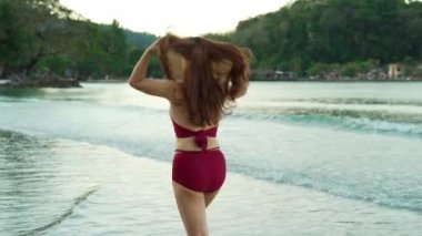 Tayland 'ın Koh Chang adasındaki deniz sahilinde mayo giymiş mutlu genç bir kadın yürüyor.