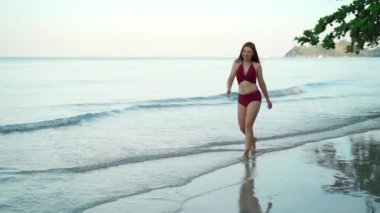 Tayland 'ın Koh Chang adasındaki deniz sahilinde mayo giymiş neşeli bir kadının ağır çekimde yürümesi.