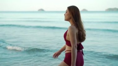 Tayland 'ın Koh Chang adasındaki deniz sahilinde mayo giymiş mutlu genç bir kadın yürüyor.