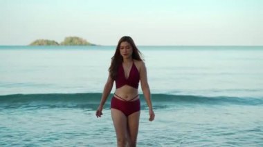 Tayland 'ın Koh Chang adasındaki deniz sahilinde mayo giymiş mutlu genç bir kadın yürüyor.
