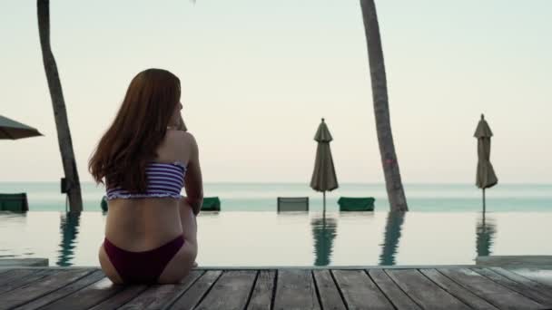 Junge Frau Badeanzug Sitzt Auf Dem Hölzernen Rand Des Swimmingpools — Stockvideo