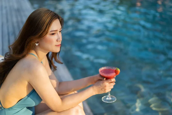 水着姿の若い女性がプールサイドで新鮮なカクテルを楽しみ — ストック写真