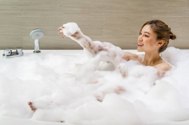Genç kadın rahatlıyor ve köpükle banyo yapıyor.