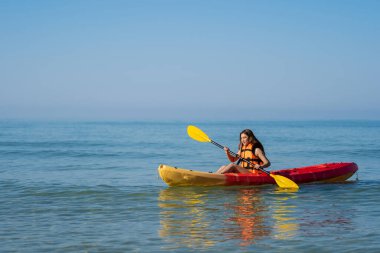 Can yeleği giymiş bir kadın denizdeki bir kano teknesinde kürek çekiyor.