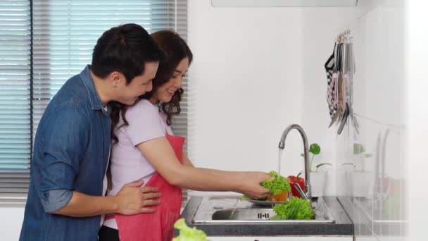Szczęśliwa Młoda Para Myjąca Warzywa Zlewie Kuchni Domu Mężczyzna Przytula — Wideo stockowe