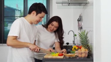 Genç çift evdeki mutfakta sağlıklı yemek hazırlamak için sebze kesiyor.