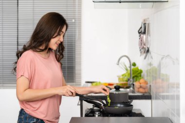 Mutlu genç bir kadın evdeki mutfakta yemek pişiriyor ve yemek hazırlıyor.