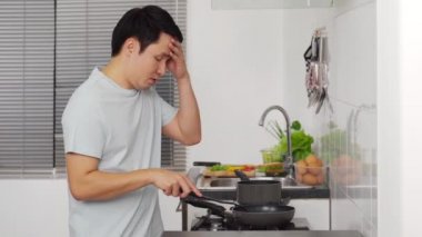 Yorgun genç adam evde yemek pişiriyor ve yemek hazırlıyor.