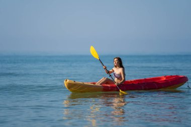 Mayo giymiş bir kadın denizde bir kano teknesinde kürek çekiyor.