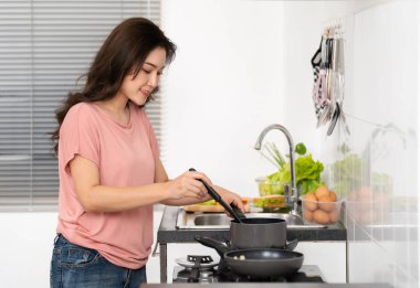 Mutlu genç bir kadın evdeki mutfakta yemek pişiriyor ve yemek hazırlıyor.