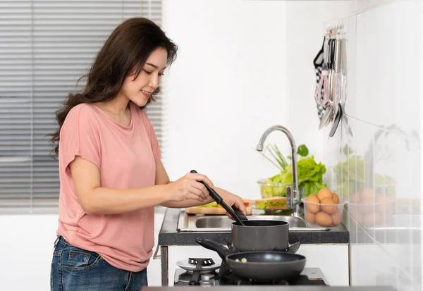 Mutlu genç bir kadın evdeki mutfakta yemek pişiriyor ve yemek hazırlıyor.