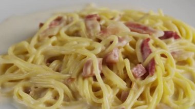 Beyaz tabakta kremalı carbonara spagettisi, döner atış.
