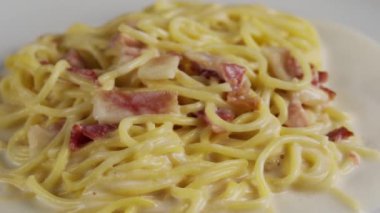 Beyaz tabakta kremalı carbonara spagettisi, döner atış.