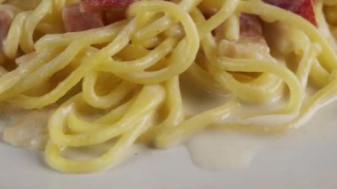 Carbonara spagettisini beyaz bir tabakta kremayla kapat. Döner atış.