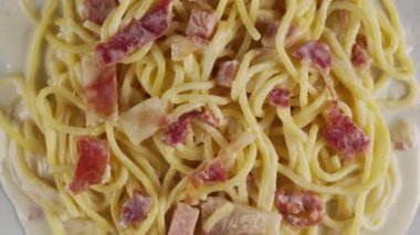 Beyaz tabakta kremalı carbonara spagettisi, döner atış.