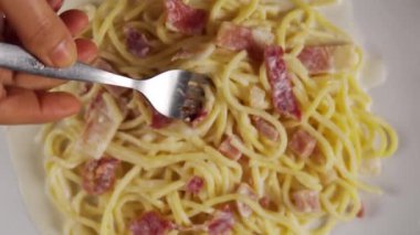 Çatal beyaz tabakta carbonara spagettisi çeviriyor.