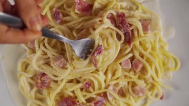 Çatalın yavaş çekimde beyaz bir tabakta carbonara spagettisi dönüyor.