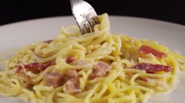 Çatal beyaz tabakta carbonara spagettisi çeviriyor.