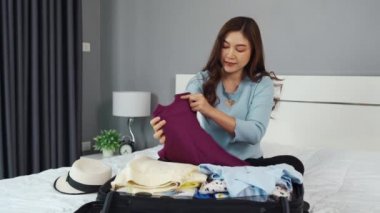 Genç bir kadın evde bir yatakta giysilerini hazırlıyor ve bavula koyuyor. Tatil seyahati konsepti.