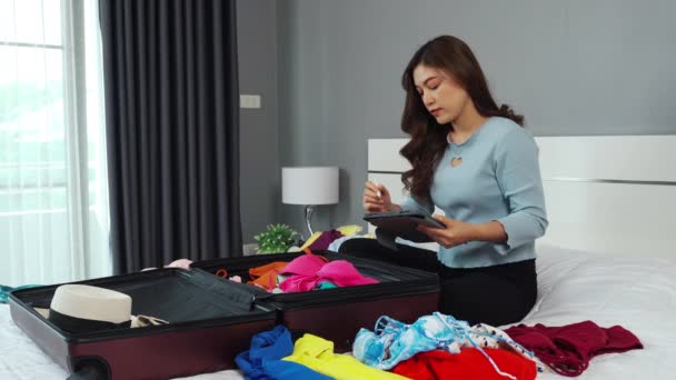 快乐的女人用平板电脑核对物品清单 在家里的床上准备好衣服 然后装进手提箱 准备度假 — 图库视频影像