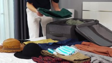 Evdeki yatakta giysileri hazırlayan ve bavula koyan adam, tatil seyahati konsepti.