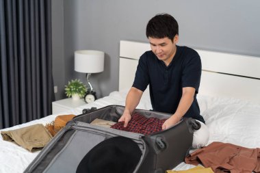 Genç adam elbiselerini hazırlıyor ve bavula koyuyor evde yatakta, tatil seyahati konsepti.