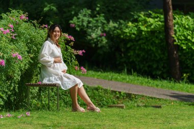 Mutlu hamile kadın parkta bankta oturuyor. 