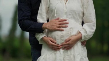 Adam hamile karısını kucaklıyor ve parkta karnını okşuyor. Evli çift bebek bekliyor..
