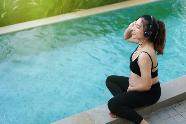 Young Pregnant Woman Sitting Edge Swimming Pool While Listening Music — Stok fotoğraf