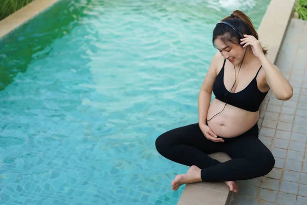 Young Pregnant Woman Sitting Edge Swimming Pool While Listening Music — Stockfoto