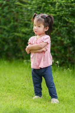 Çimen tarlasında kolları çapraz olan küçük bir kız.