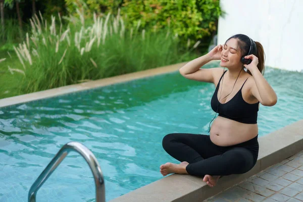 Young Pregnant Woman Sitting Edge Swimming Pool While Listening Music — Fotografia de Stock