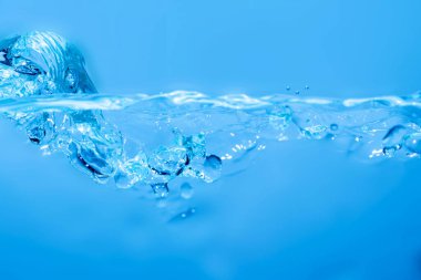 Blue water splashes the wave surface with bubbles of air on white background.