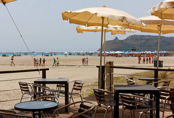 КАГЛИАРИ, Италия - 07 июля 2021 года: Жизнь на пляже Поэтто недалеко от города, со столиками на переднем плане