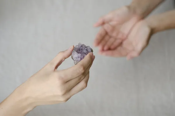 Mujeres manos dando un cristal de amatista uno a otro Imagen de stock