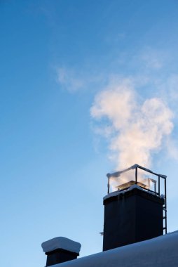 Evin bacasından duman çıkıyor, soğuk kış gününde ısınıyor, açık mavi gökyüzü.