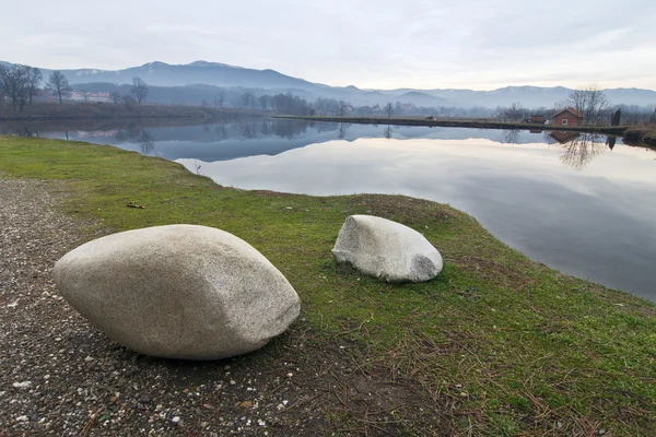 Rocks on the shore of the lake. house in the distance — Stock Photo, Image