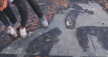 İşçiler, bir binanın terasına yapışan bozulmuş bituminöz kılıfı çıkarıyorlar. Sonra yeni bir su geçirmez katman yerleştirilecek..