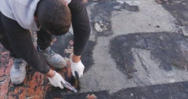İşçiler, bir binanın terasına yapışan bozulmuş bituminöz kılıfı çıkarıyorlar. Sonra yeni bir su geçirmez katman yerleştirilecek..
