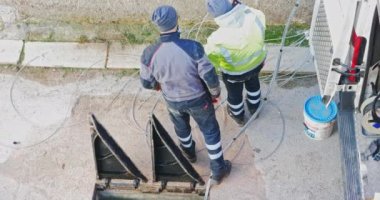 İşçiler yeraltı kablo kanallarına fiber optik kablolar yerleştirip geniş bant telekomünikasyon ağı oluşturuyorlar. Üçgen döküm demir rögar kapaklarını aç