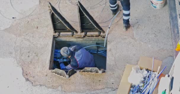 労働者は広帯域通信ネットワークを作成するために地下ケーブルダクトに光ファイバーケーブルを挿入する 三角形の鋳鉄マンホールカバーを開く — ストック動画
