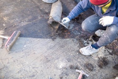 İşçiler, bir binanın terasına yapışan bozulmuş bituminöz kılıfı çıkarıyorlar. Sonra yeni bir su geçirmez katman yerleştirilecek..
