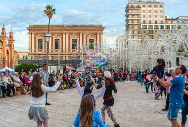 Bari, Italy - February 9, 2018: street artist making children play with big soap bubbles in a square in Bari. In the background the Margherita theatre