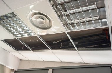 İnşaat işçisi asılmış tavanı alçıpanla birleştiriyor ve alçıpanı tornavidayla tavandaki metal çerçeveye yerleştiriyor..