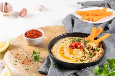 Humusa batırılmış havuç çubuğuyla seramik fiyonk içinde nefis humus. Beyaz arkaplanda renkli abur cubur kompozisyonu.