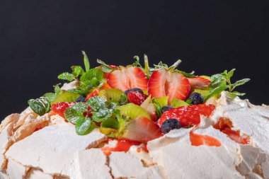 Kremalı Pavlova pastası ve taze yaz meyveleri ve ahşap arka planda kivi. Pavlova tatlısını orman meyvesi ve nane ile kapat. Yemek fotoğrafçılığı