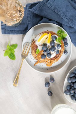 Sağlıklı yaz kahvaltısı, taze böğürtlen, limon, yoğurt ve fıstık ezmeli ev yapımı Amerikan krepleri. Sabah açık gri taş arka plan.