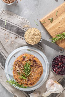 Çiğ vejetaryen burger, kinoalı, kırmızı tavuk, sebze ve biberiye yapraklı mutfak tezgahı.