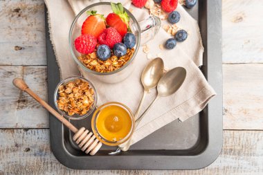 Kavanozda fındıklı, yoğurtlu ve kırmızı meyve meyveli granola. Müsli, yoğurt, kırmızı meyve ve bal ile kahvaltı, beyaz mutfak arka planı..